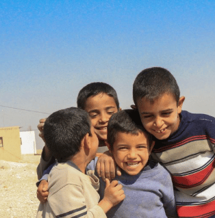 Group of smiling boys standing outdoors under a clear blue sky.