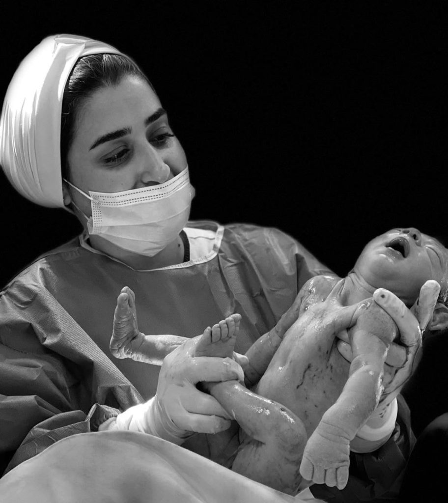 Doctor holding a newborn baby immediately after delivery in a black-and-white photo.