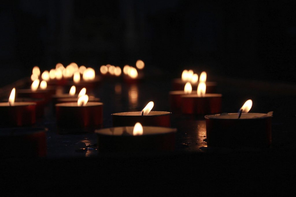 Multiple lit tealight candles glowing in the dark.