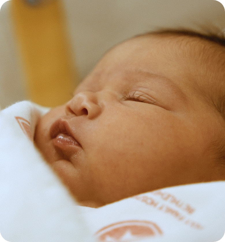 Close-up of a sleeping newborn baby wrapped in a white blanket.